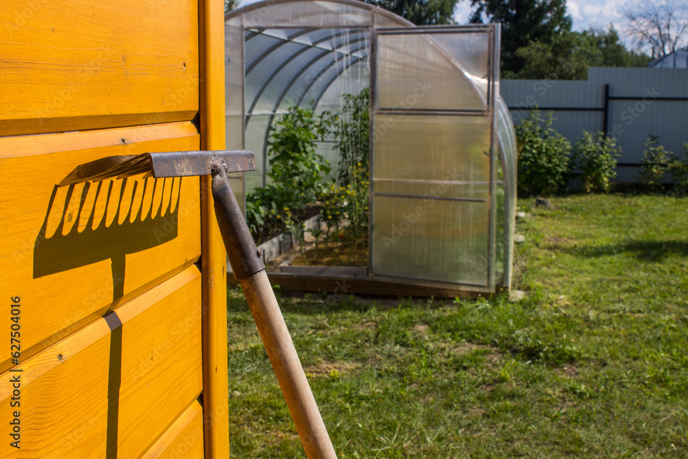 An old rusty rake is leaning against a yellow wooden wall and a contrasting shadow and copy space. Concept - gardening and countryside An old rusty rake is leaning against a yellow wooden wall and a contrasting shadow and copy space. Concept - gardening and countryside