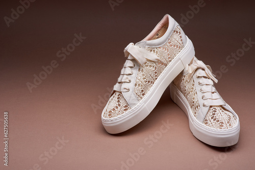 Stylish pastel knitted design sneakers with white thick rubber soles on a gradient brown background. One shoe stands on another. The concept of modern footwear