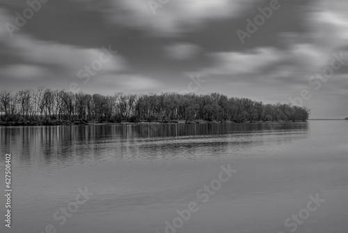 View of a wooded island across a still body of water, reflection, clouds, nobody