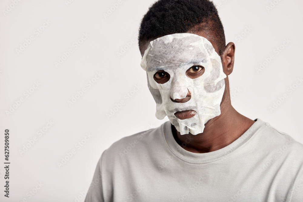 Close-up studio portrait of young black man with moisturizing paper mask on his face. Happy African American millennial man uses beauty products in his skincare routine to maintain healthy look. Close-up studio portrait of young black man with moisturizing paper mask on his face. Happy African American millennial man uses beauty products in his skincare routine to maintain healthy look.