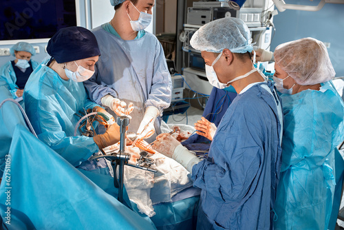 Top view of surgeons team during complex surgical operation in a bright sterile operating room. Doctors leaned over patient using modern surgical instruments and clamps. Saving patient's life.