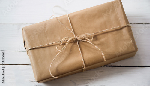 Close up Christmas style rustic brown paper package tied up with strings. White wood floor background.