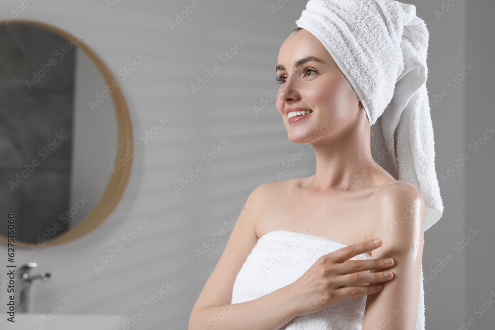 Happy woman applying body oil onto arm in bathroom, space for text Happy woman applying body oil onto arm in bathroom, space for text