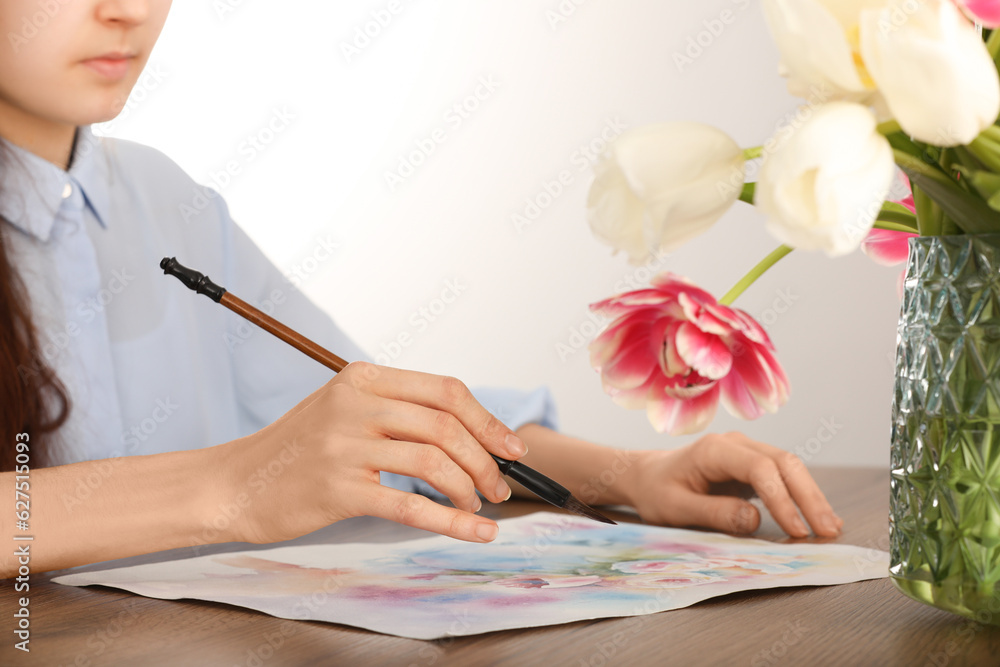 Woman painting flowers with watercolor at wooden table indoors, closeup. Creative artwork