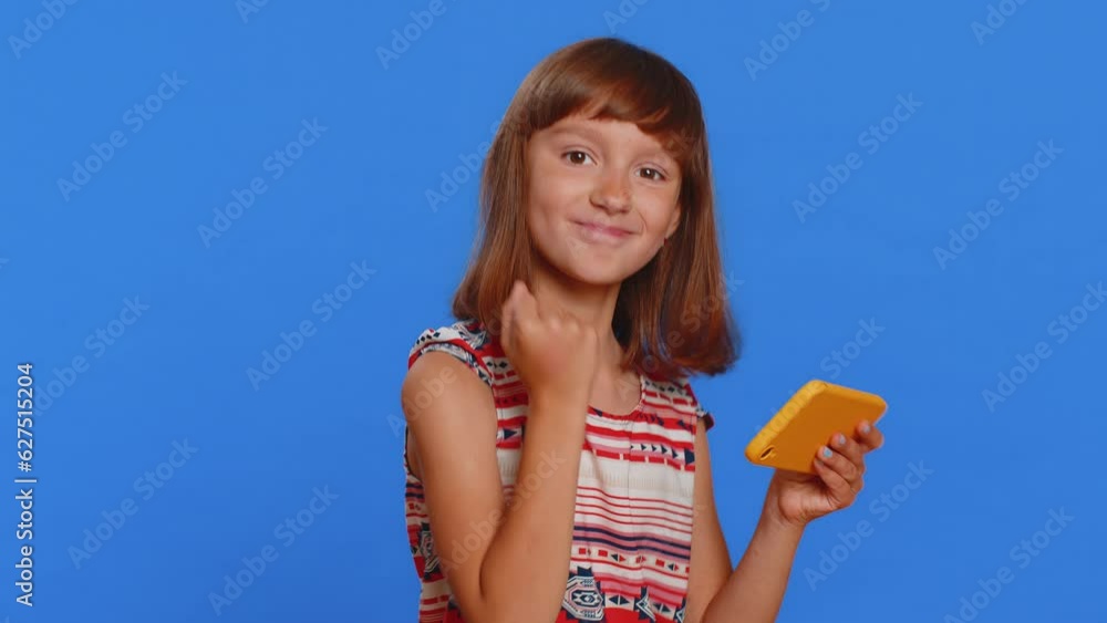 Worried funny young school girl enthusiastically playing racing or shooter video games on smartphone. Preteen Caucasian child kid using smartphone gadget app with drive simulator on blue background Worried funny young school girl enthusiastically playing racing or shooter video games on smartphone. Preteen Caucasian child kid using smartphone gadget app with drive simulator on blue background