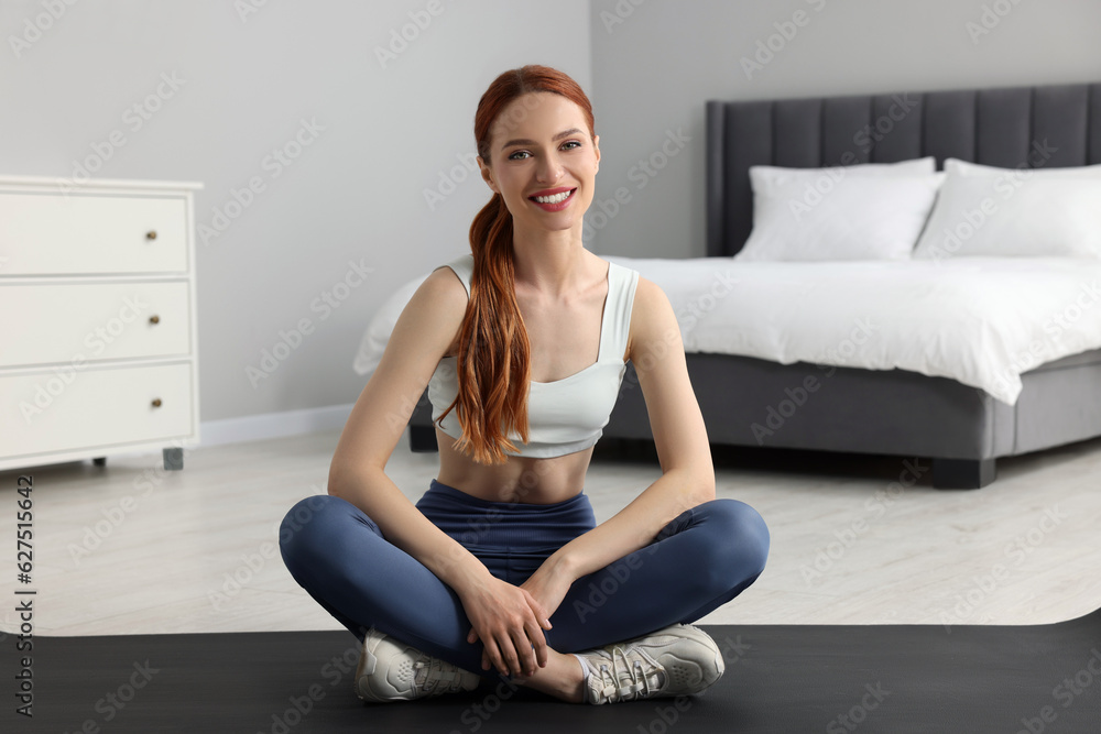 Young woman in sportswear sitting on fitness mat in bedroom Young woman in sportswear sitting on fitness mat in bedroom