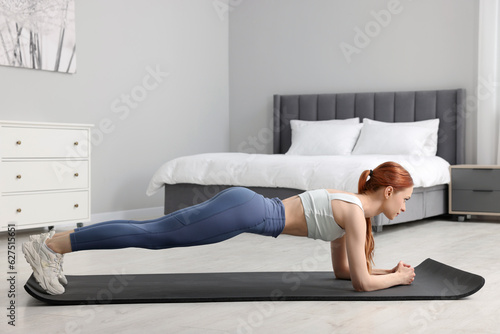 Fototapeta Naklejka Na Ścianę i Meble -  Young woman in sportswear doing exercises on fitness mat in bedroom