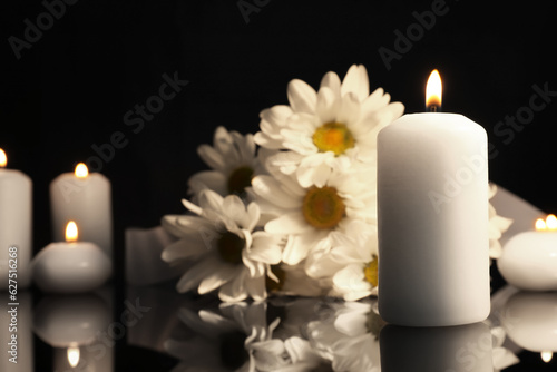 White chrysanthemum flowers and burning candles on black mirror surface in darkness, space for text. Funeral symbols