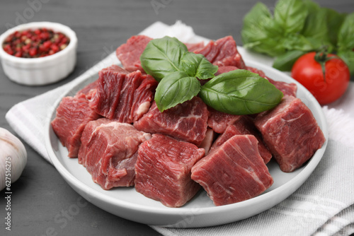 Cut fresh beef meat with basil leaves on grey table, closeup