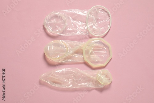 Unrolled female and male condoms on light pink background, flat lay. Safe sex