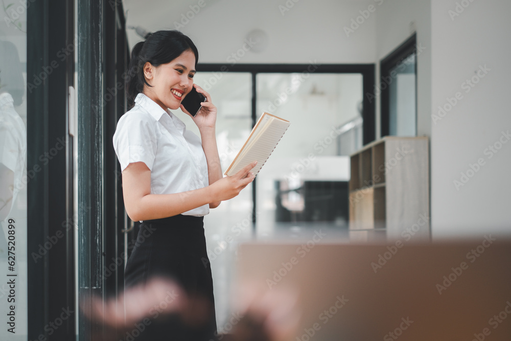 Fototapeta premium Happy businesswoman talking on mobile phone while analyzing weekly schedule in her paper.