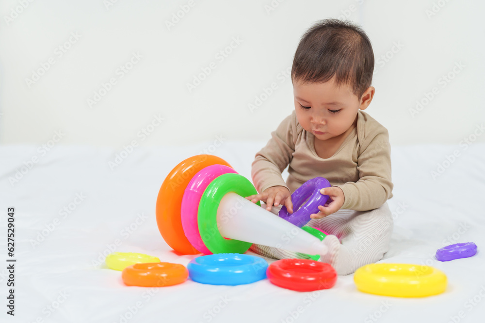 infant baby playing the pyramid toy with colored rings on bed infant baby playing the pyramid toy with colored rings on bed