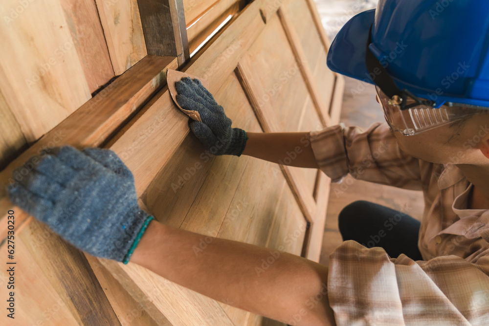 An Asian carpenter is polishing a piece of work with fine sandpaper by hand. Wear a helmet and goggles to prevent dust. An Asian carpenter is polishing a piece of work with fine sandpaper by hand. Wear a helmet and goggles to prevent dust.