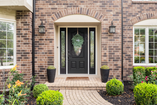 The front door of a brick home with a black front door and a stone path sidewalk. photo