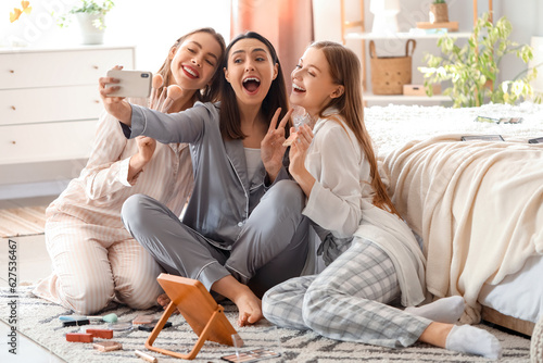 Young women with applied makeup taking selfie in bedroom