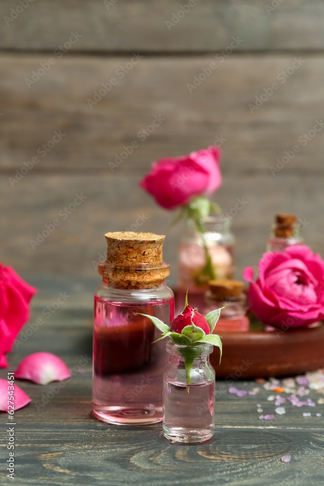 Bottles of cosmetic oil with rose extract and flowers on wooden table Bottles of cosmetic oil with rose extract and flowers on wooden table