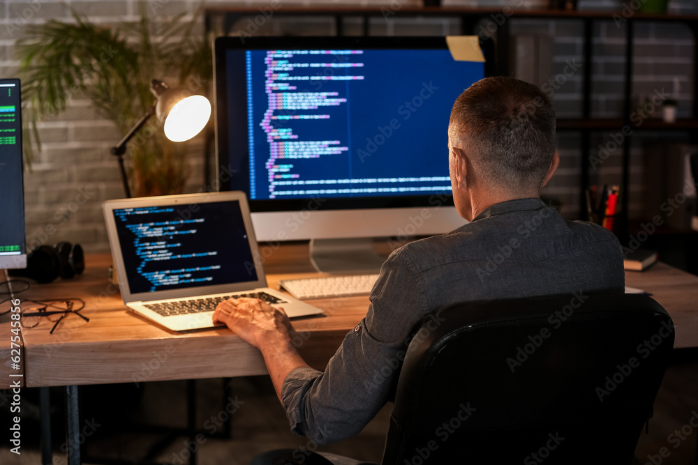 Mature male programmer working in office at night, back view Mature male programmer working in office at night, back view