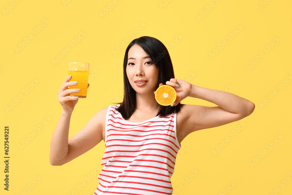 Beautiful Asian woman with orange and glass of juice on yellow background Beautiful Asian woman with orange and glass of juice on yellow background