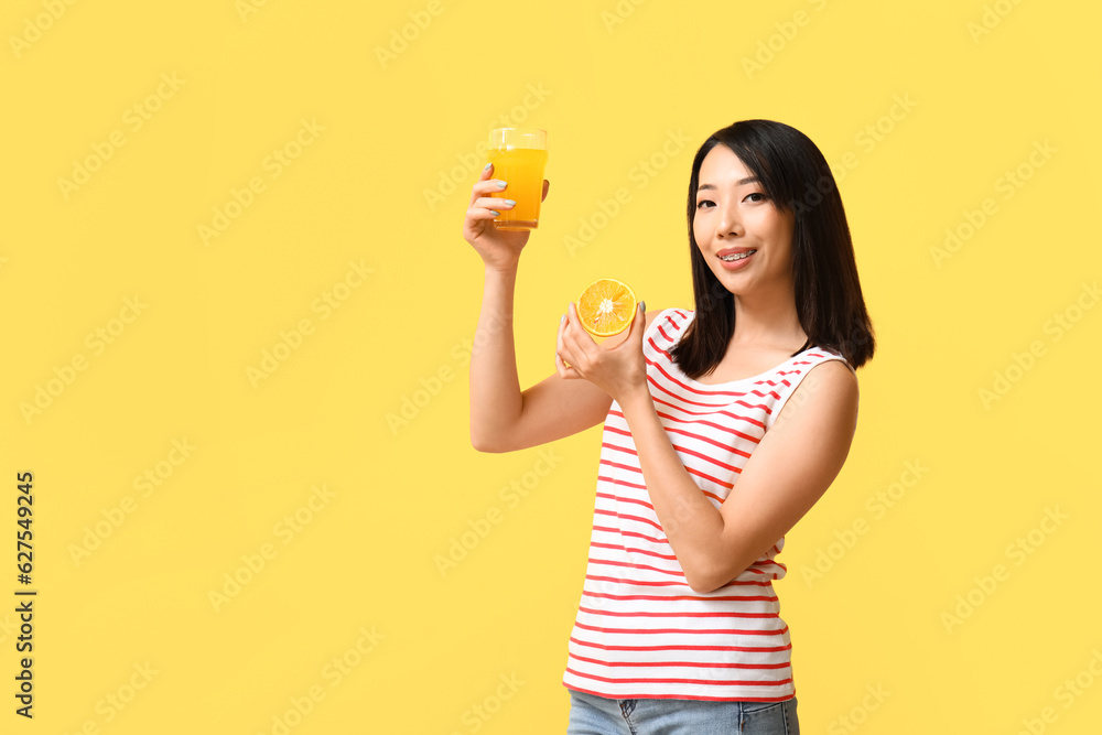 Beautiful Asian woman with orange and glass of juice on yellow background Beautiful Asian woman with orange and glass of juice on yellow background