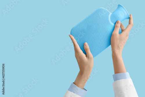 Fotografie Female doctor's hands with hot water bottle on blue background