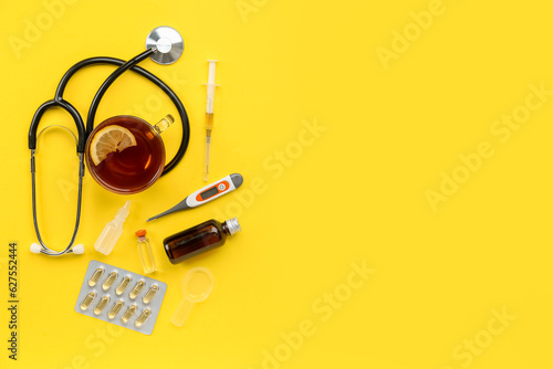 Stethoscope, cup of tea, pills and thermometer on yellow background