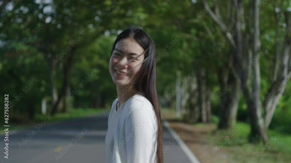Happy asian girl with flowing hair jumping on green park road in sunny day outdoor, Beautiful female with long hair laughing and walks on the road at sunset, Cute woman playfully smiles outdoor. Happy asian girl with flowing hair jumping on green park road in sunny day outdoor, Beautiful female with long hair laughing and walks on the road at sunset, Cute woman playfully smiles outdoor.