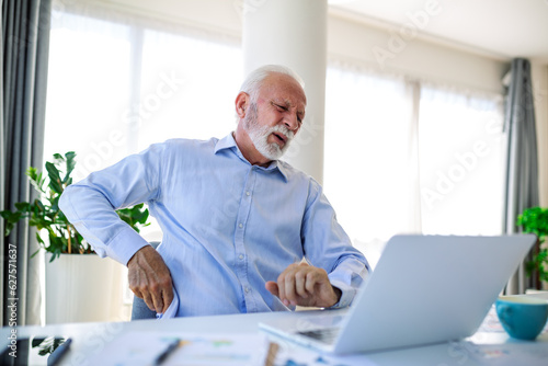 Senior businessman working sitting at desk suffers from lower back pain. Damage of intervertebral discs, spinal joints, compression of nerve roots caused by wrong posture and sedentary work