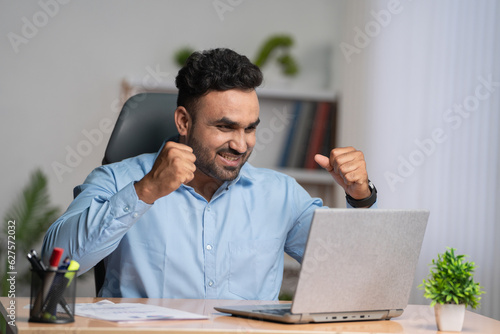 Excited Indian corporate employee celebrating or businessman after sales achievement at office - concept of loan approval, good news and promotional letter.