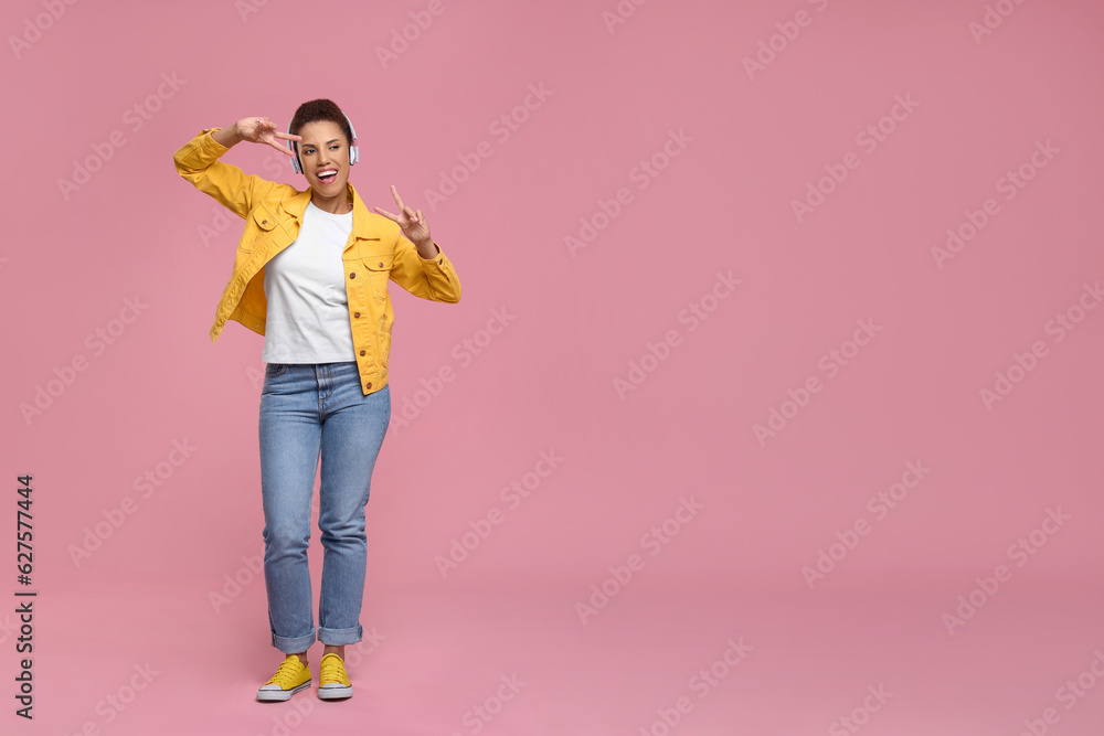 Happy young woman in headphones dancing on pink background. Space for text Happy young woman in headphones dancing on pink background. Space for text