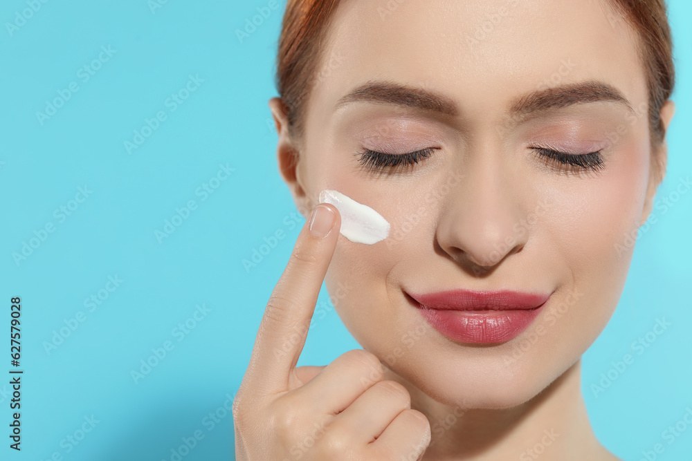 Beautiful young woman with sun protection cream on her face against light blue background, closeup. Space for text