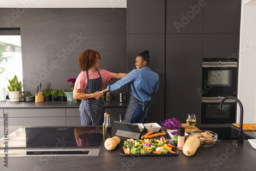 Happy diverse couple in aprons preparing meal having fun dancing in kitchen