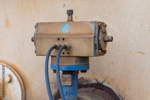Photograph of an old and dirty motor controller on a water truck bolted to a blue steel flange and pipe with control cables connected to the control box