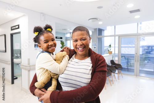 Portrait of happy african american mother and daughter in waiting room at hospital