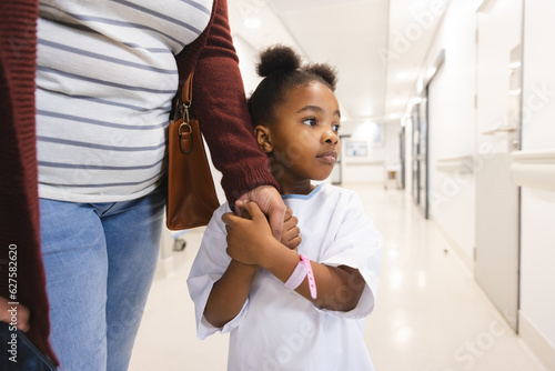African american girl patient and her mother holding hands in corridor at hospital