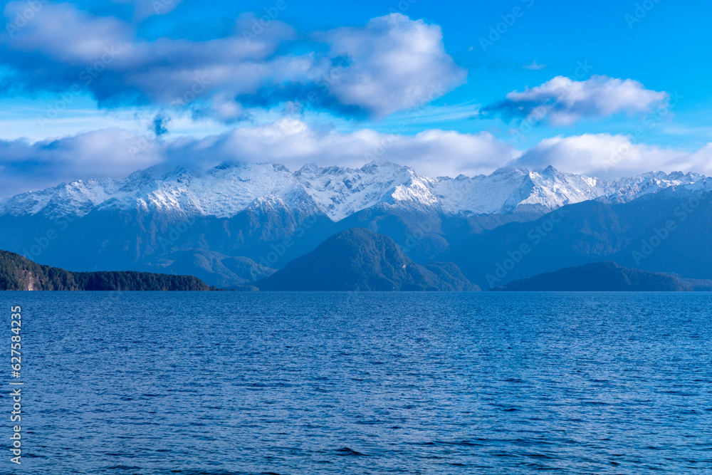 Photograph of a large blue lake and snow-capped mountain range while driving from Te Anau in Fiordland to Manapouri on the South Island of New Zealand