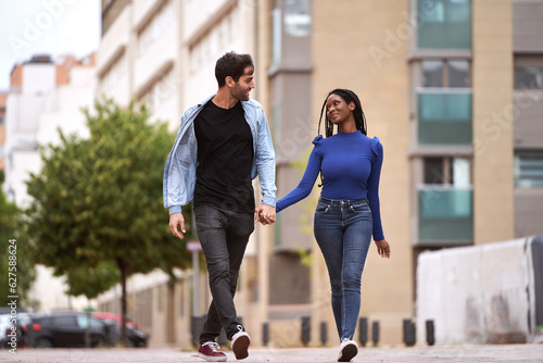 Multi-ethnic couple smiling as they walk together holding hands on the street.. Relationship concept.
