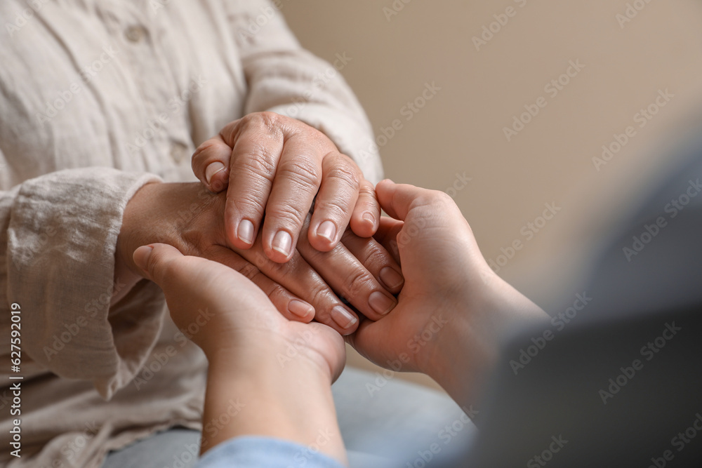 Woman holding hands with her mother on beige background, closeup