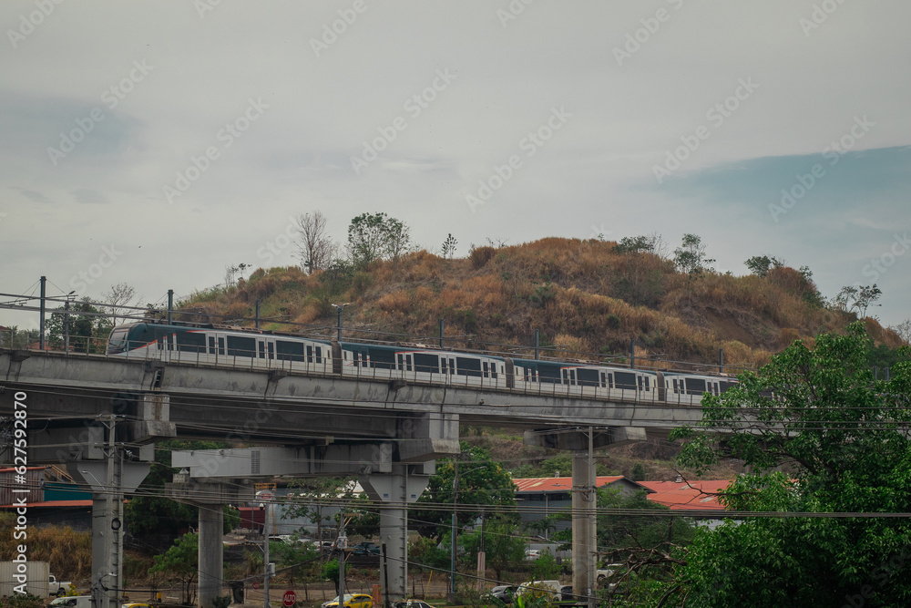 New panama metro system is being built. New metro rail car is arriving to station that leads to the aeroport. Suspended metro over the bridge in Panama suburb on a cloudy day.