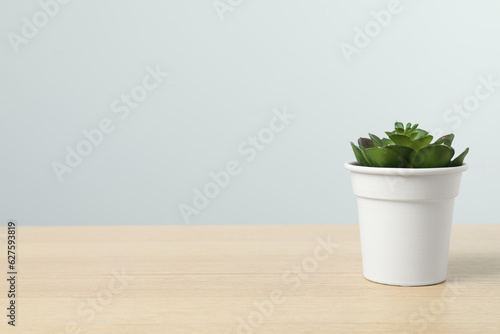 Beautiful artificial plant in flower pot on wooden table against light grey background, space for text © New Africa