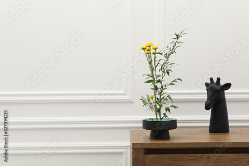 Stylish ikebana with beautiful yellow flowers  green branch and decor carrying cozy atmosphere at home  space for text