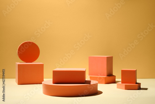 Many orange geometric figures on table against yellow background  space for text. Stylish presentation for product