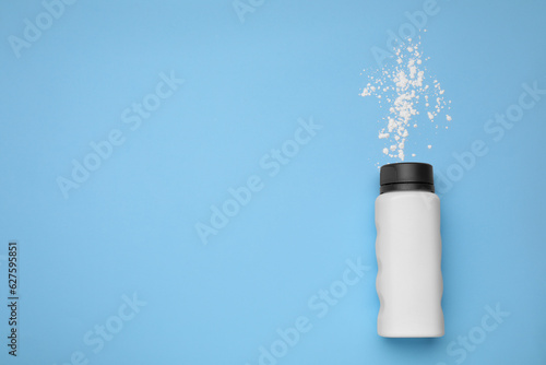 Bottle and scattered dusting powder on light blue background  top view with space for text. Baby cosmetic product