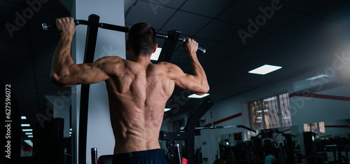 Back view of shirtless man with pull-ups in gym. 