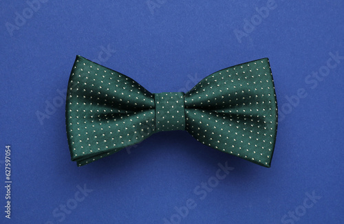 Stylish green bow tie with polka dot pattern on blue background, top view