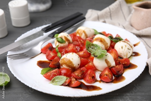 Tasty salad Caprese with tomatoes, mozzarella balls, basil and balsamic vinegar on grey table, closeup