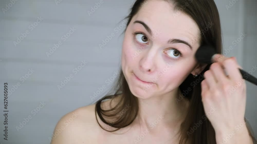 The girl does her nude make-up by applying pink blush with a large brush. A beautiful 30s woman putting on her makeup. A winter color type. Beauty model. Healthy appearance and white skin. Close-up. The girl does her nude make-up by applying pink blush with a large brush. A beautiful 30s woman putting on her makeup. A winter color type. Beauty model. Healthy appearance and white skin. Close-up.