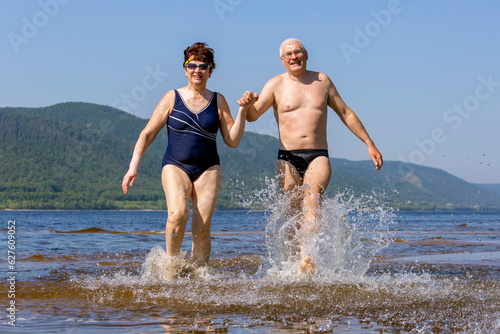 beautiful mature couple runs on the water along the wild beach on a hot summer day