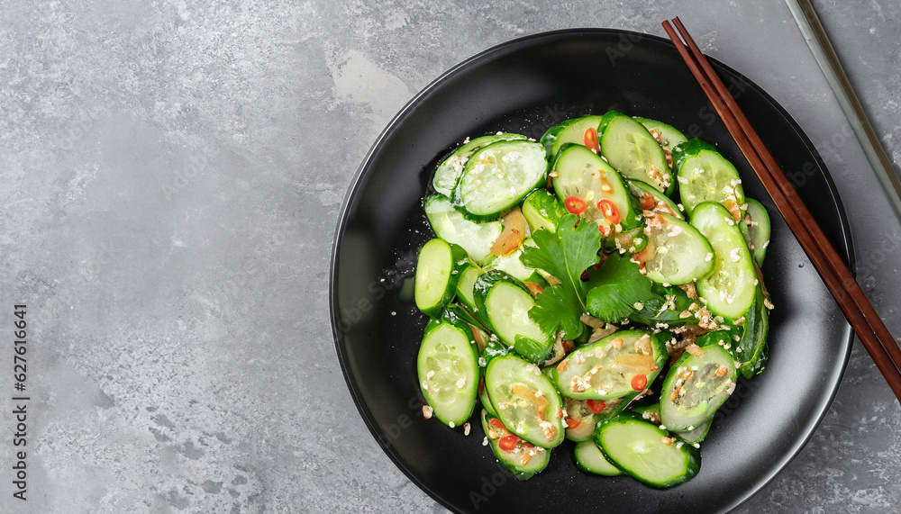 pai huang gua, Chinese Smashed Cucumber salad sprinkled with fresh coriander leaves in a black bowl with chopsticks on a concrete table, flat lay, free space pai huang gua, Chinese Smashed Cucumber salad sprinkled with fresh coriander leaves in a black bowl with chopsticks on a concrete table, flat lay, free space