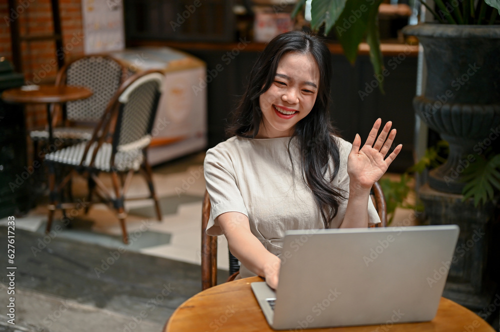 A cheerful Asian woman is having an online meeting while working remotely at a coffee shop. A cheerful Asian woman is having an online meeting while working remotely at a coffee shop.