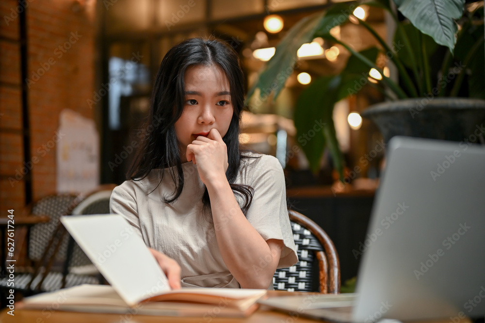 A doubtful and thoughtful Asian woman is looking at her laptop screen with a serious face A doubtful and thoughtful Asian woman is looking at her laptop screen with a serious face